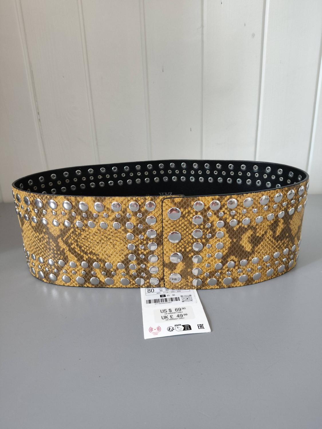 Wide yellow belt with a snake print and silver studs on a white background. Text: 80, US $69.90, UK £49.99, EAC.