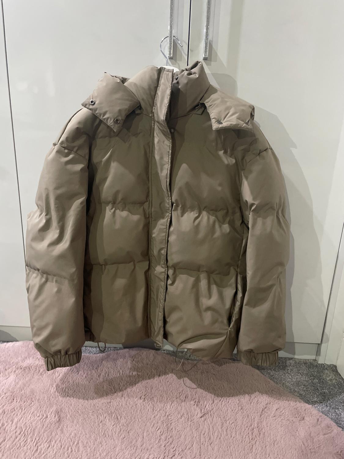Beige quilted jacket hanging on a hanger over a white door. Pink carpet background and grey floor.