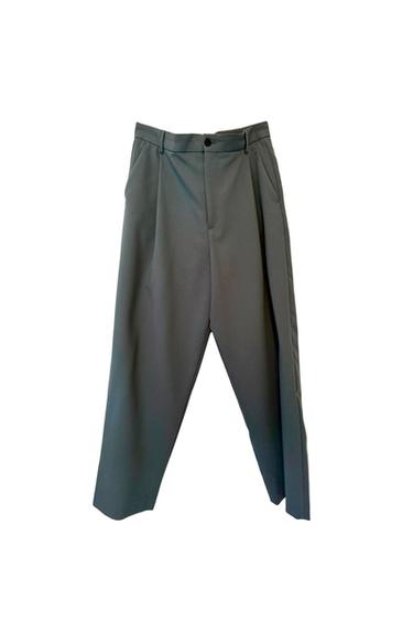 Loose-fit gray pants with front pleats and black button closure, hanging on a white background.