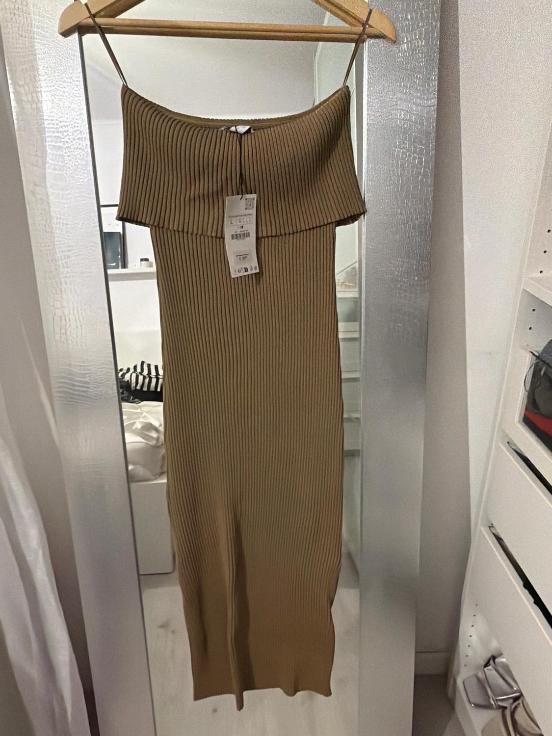 Brown ribbed knit dress hanging on a hanger in front of a mirror. Visible label in the centre of the dress.