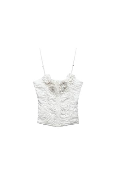 Front view of a white top with spaghetti straps and floral detailing at the neckline, ruched design throughout.