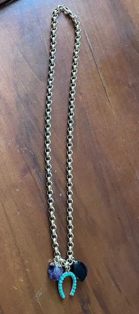Gold chain with pendants: a turquoise horseshoe and two stones, one purple and one black, on a brown wooden background.