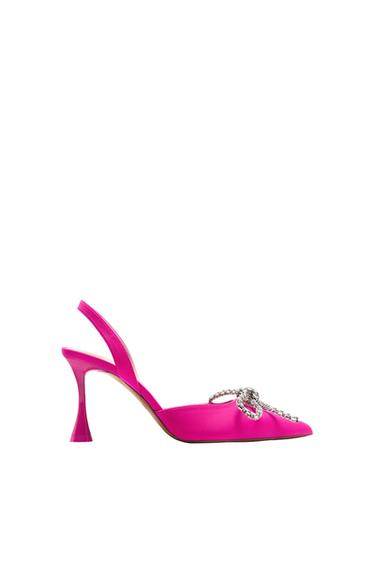 Fuchsia slingback high-heeled shoe on a white background. It features a pointed toe and a sparkly rhinestone bow on the front.
