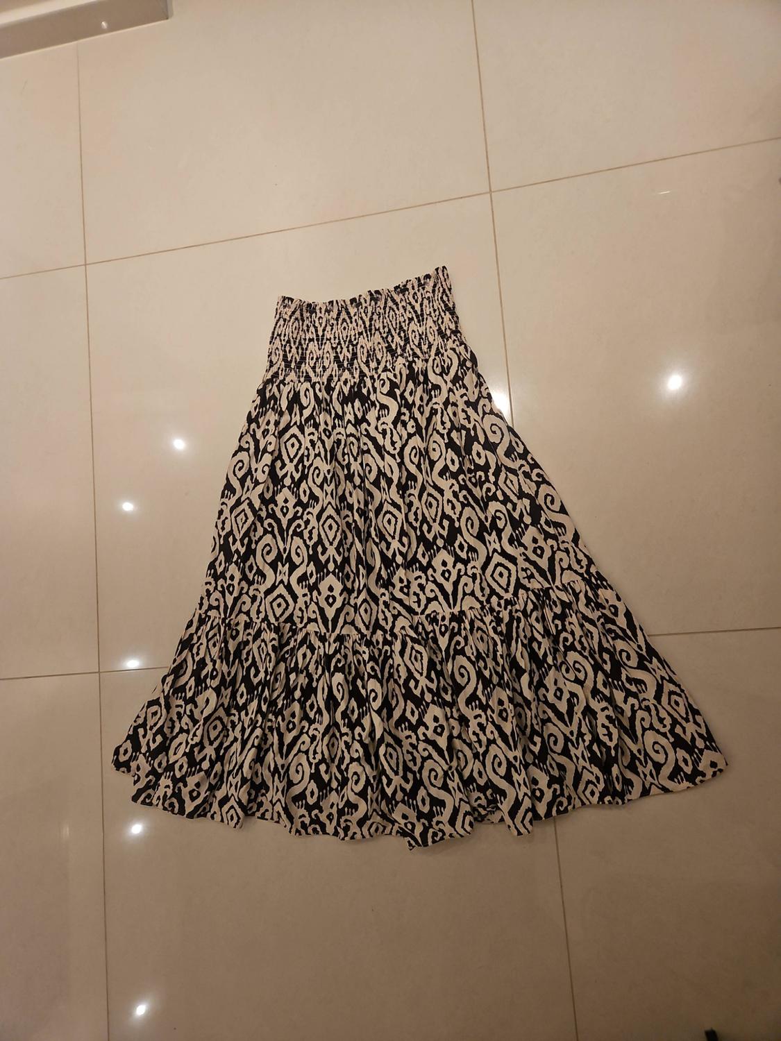 Long skirt with an elasticated waist and an abstract black-and-white pattern, laid out on a light tiled floor.