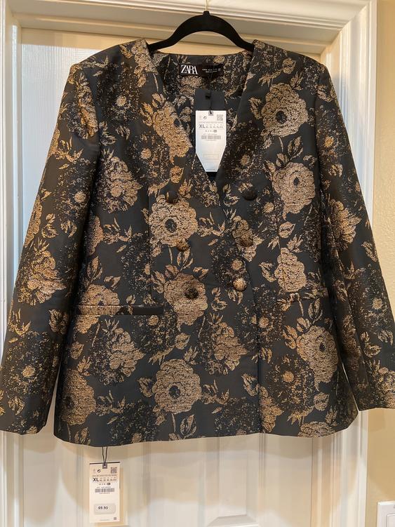 Black jacket with gold floral print, hanging on a hanger. Visible tag with size XL and price 69.90.