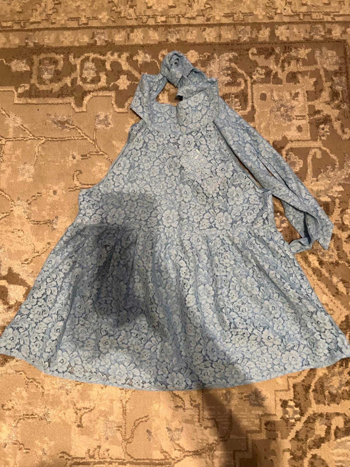 Light blue floral lace dress on a beige rug with a geometric design. Long sleeves and a tie-neck.