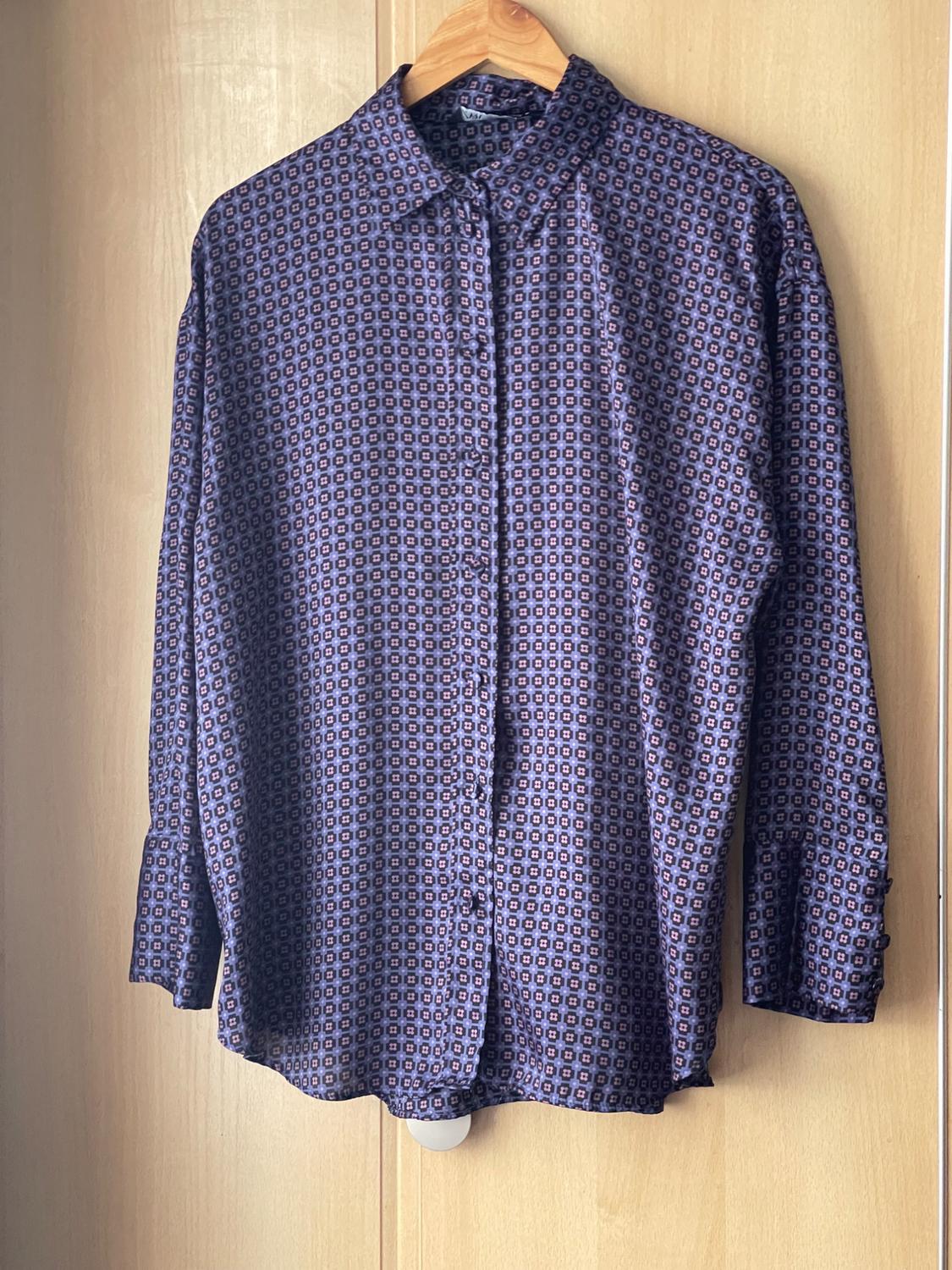 Long-sleeved shirt with a geometric print in blue and purple tones, hung on a wooden hanger against a light wooden background.