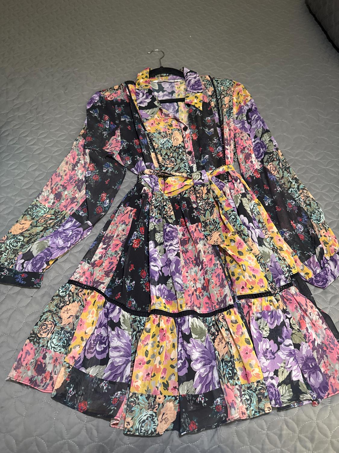 Multicolor floral dress with long sleeves and a belt, on a gray quilted comforter.
