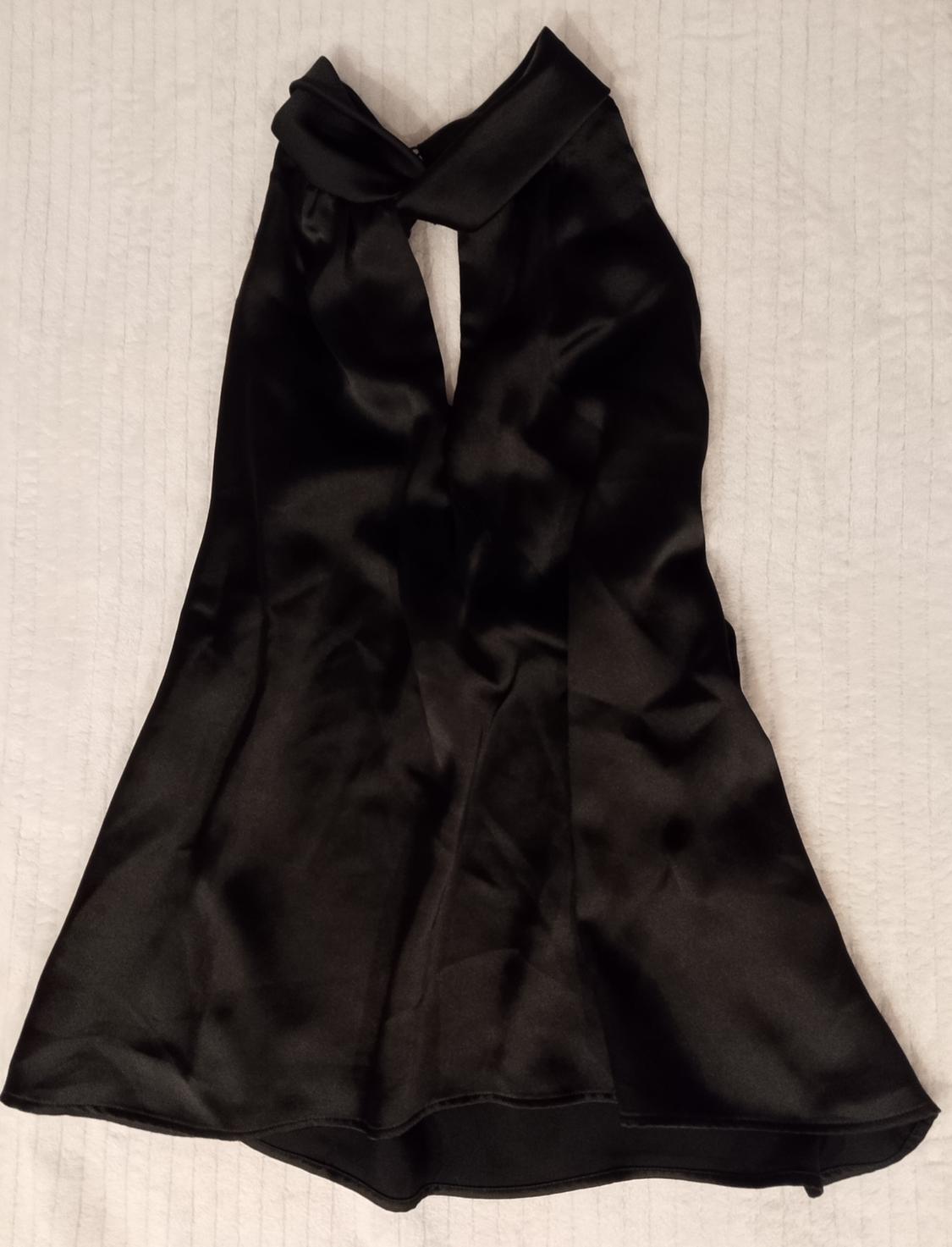 Black satin top with a crossover halter neck and V-neckline, laid out on a textured white background.