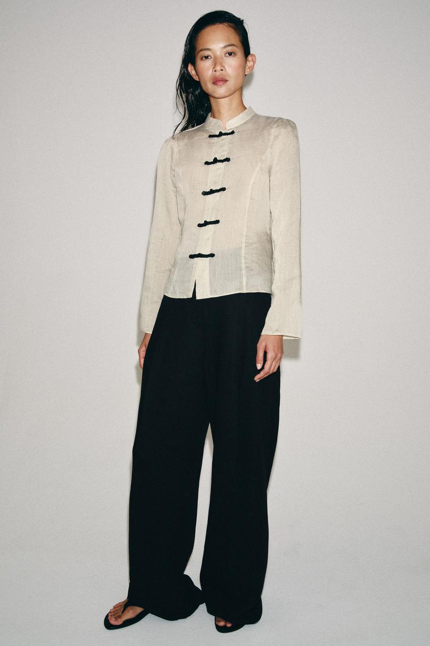 Raw striped long-sleeve shirt set with a round neck and front toggle closures, and loose black pants.