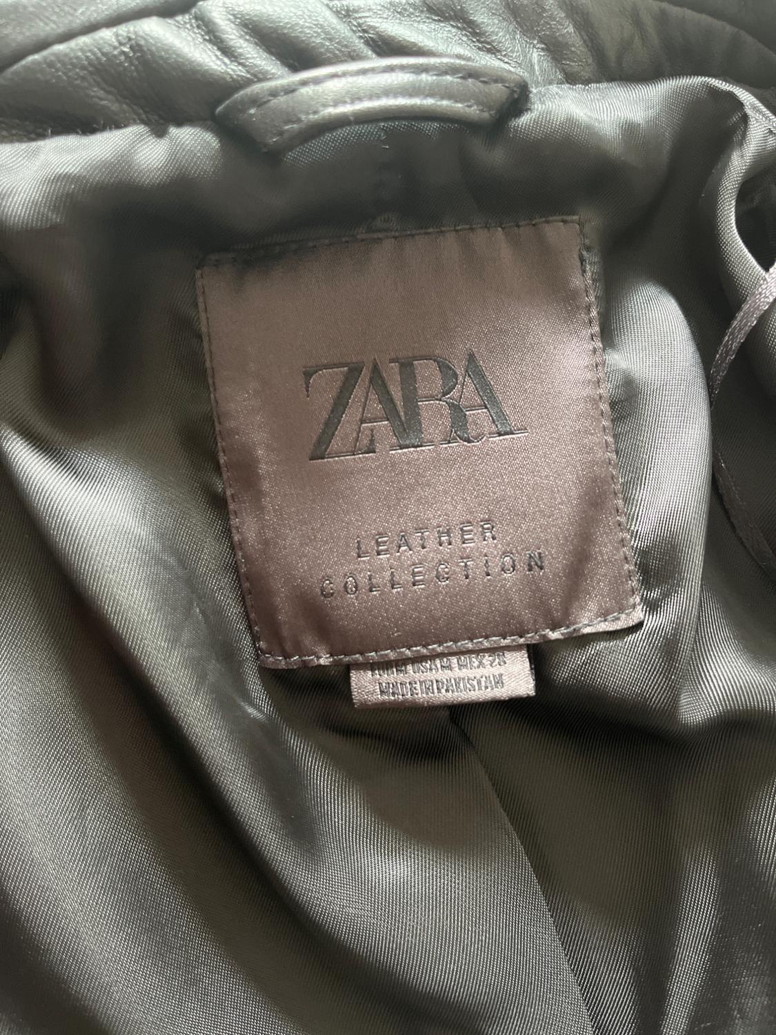 Jacket label with text "ZARA LEATHER COLLECTION" on grey fabric. Additional label indicates "MADE IN PAKISTAN".