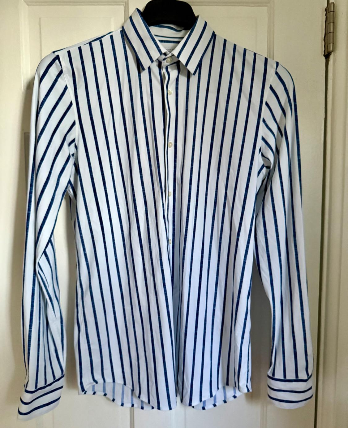 Button-down shirt with blue and white vertical stripes, hanging on a hanger against a white door.