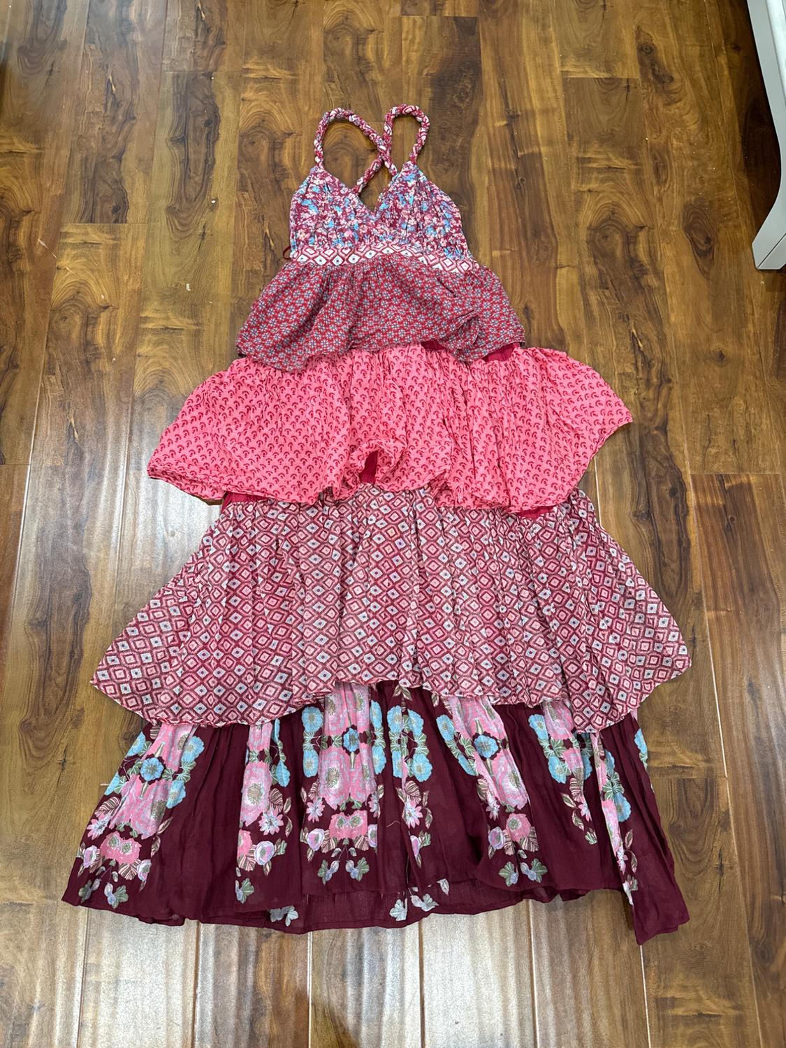 Long, cross-back strap dress with a floral and geometric print in shades of pink and burgundy, on a wooden floor.