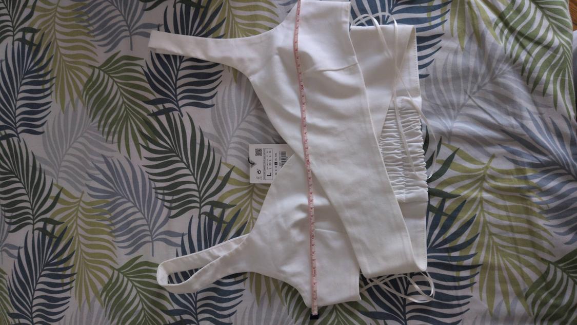 White cropped top with a size L label measured with a pink tape measure, on a fabric background with a green and grey leaf print.