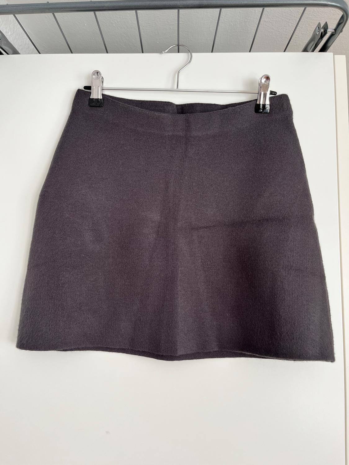 Grey mini skirt hanging on a coat hanger against a white backdrop, with visible texture and a simple design.