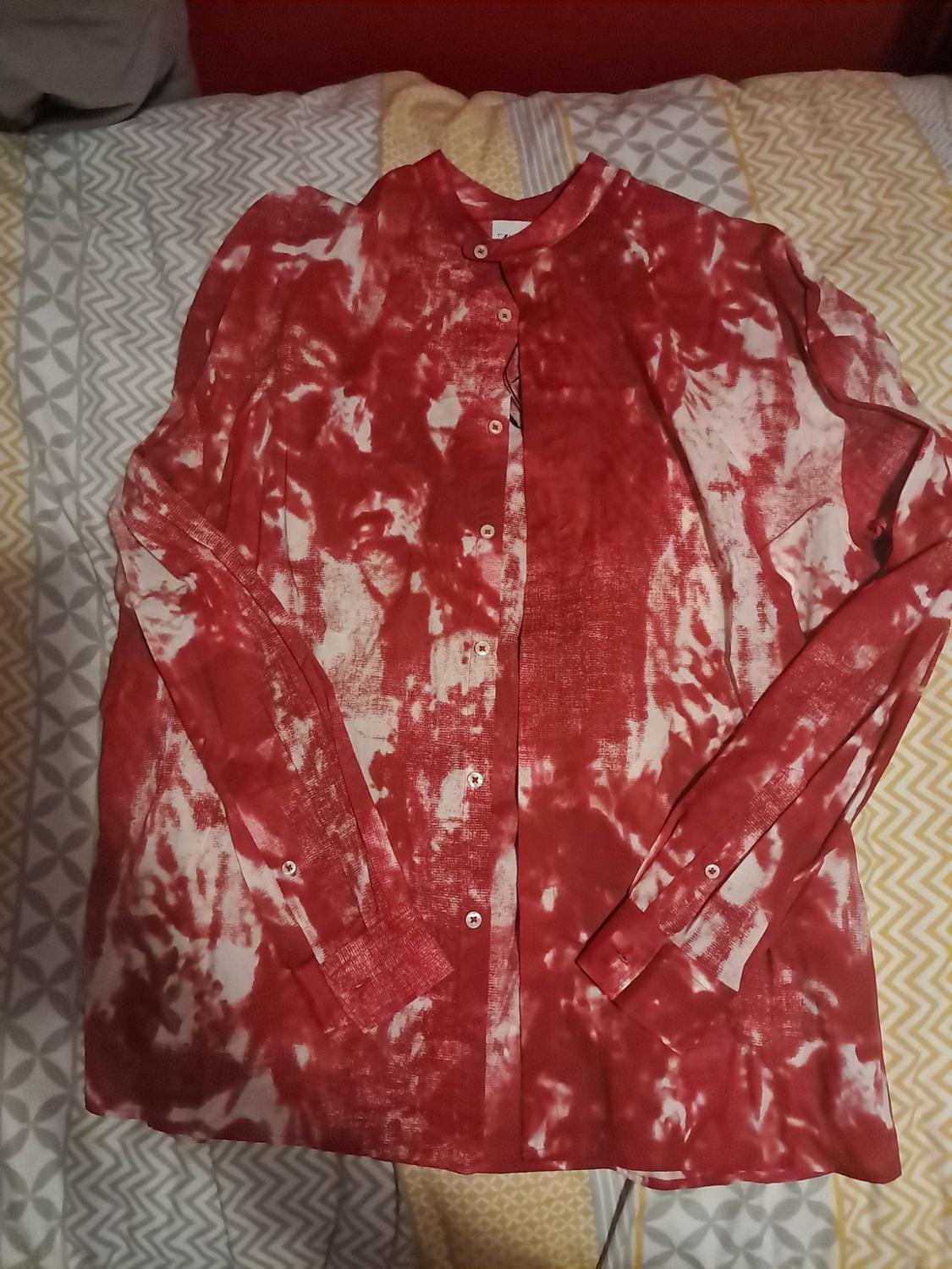 Red and white abstract-print long-sleeved button-up shirt, laid out on a bed with geometric-patterned sheets.