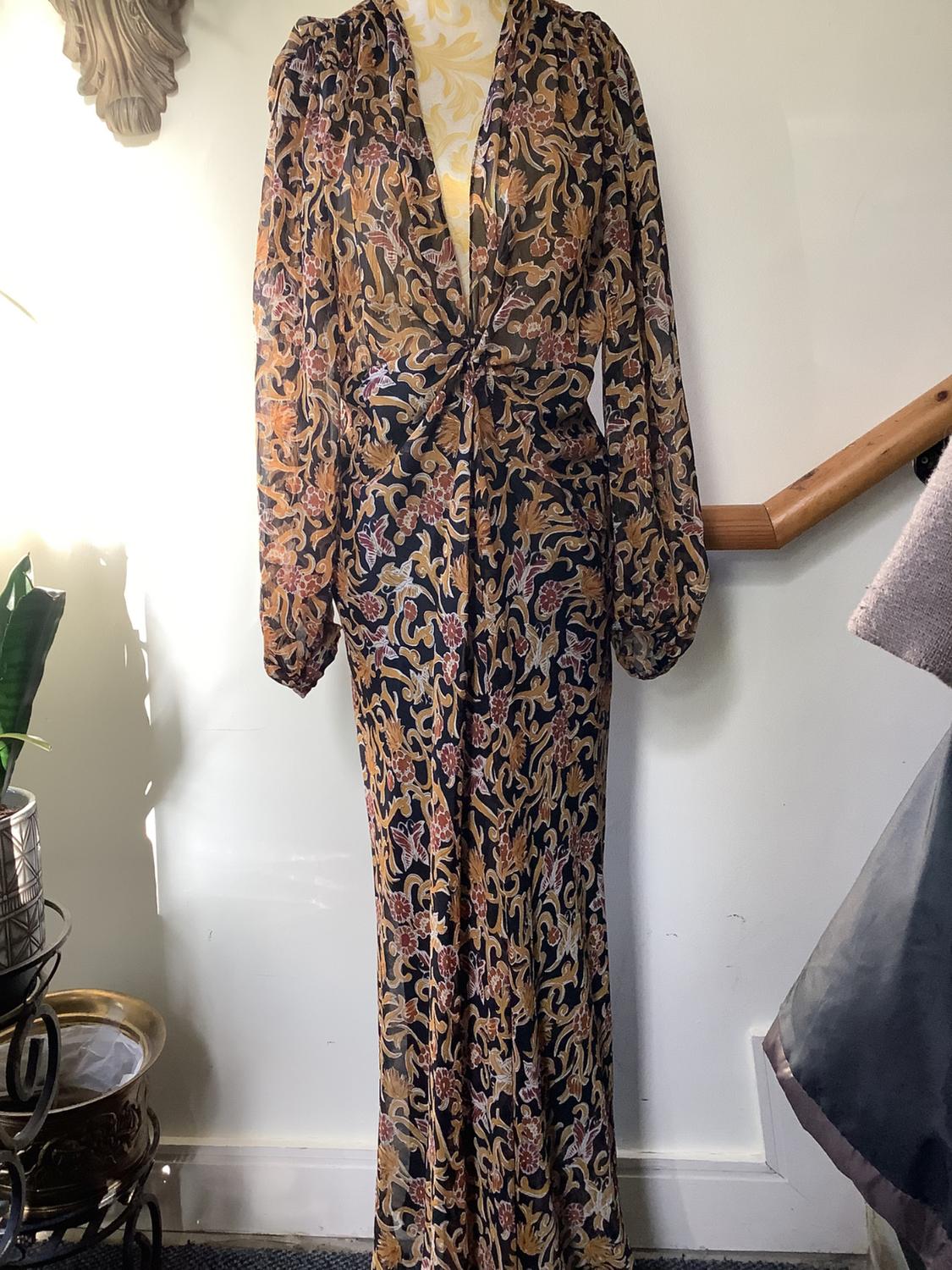 Mannequin in a long-sleeved, long dress with a floral print in brown and gold tones, in an interior with natural light.