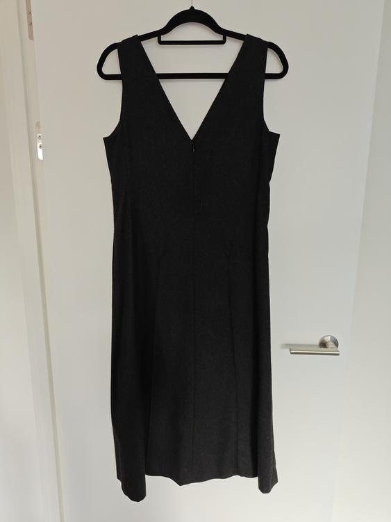 Sleeveless black dress with a V-neckline hanging on a black hanger over a white door.