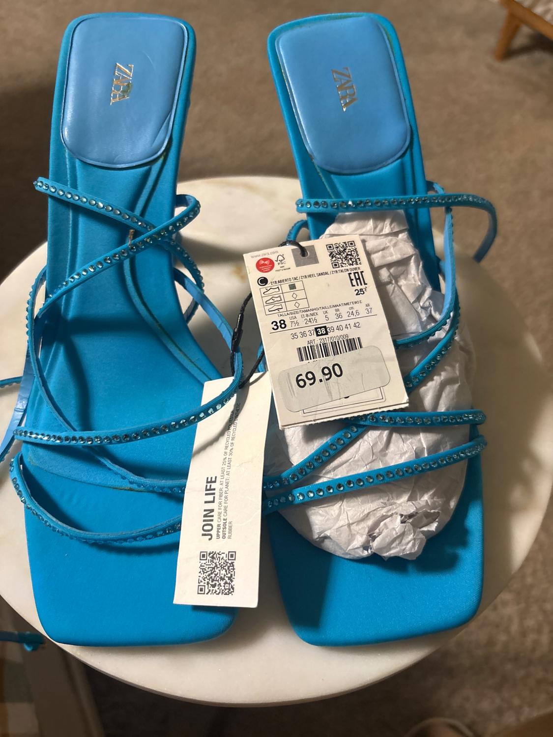 Blue sandals with decorated straps and a price tag of 69.90 on a white table. Visible text: "JOIN LIFE".