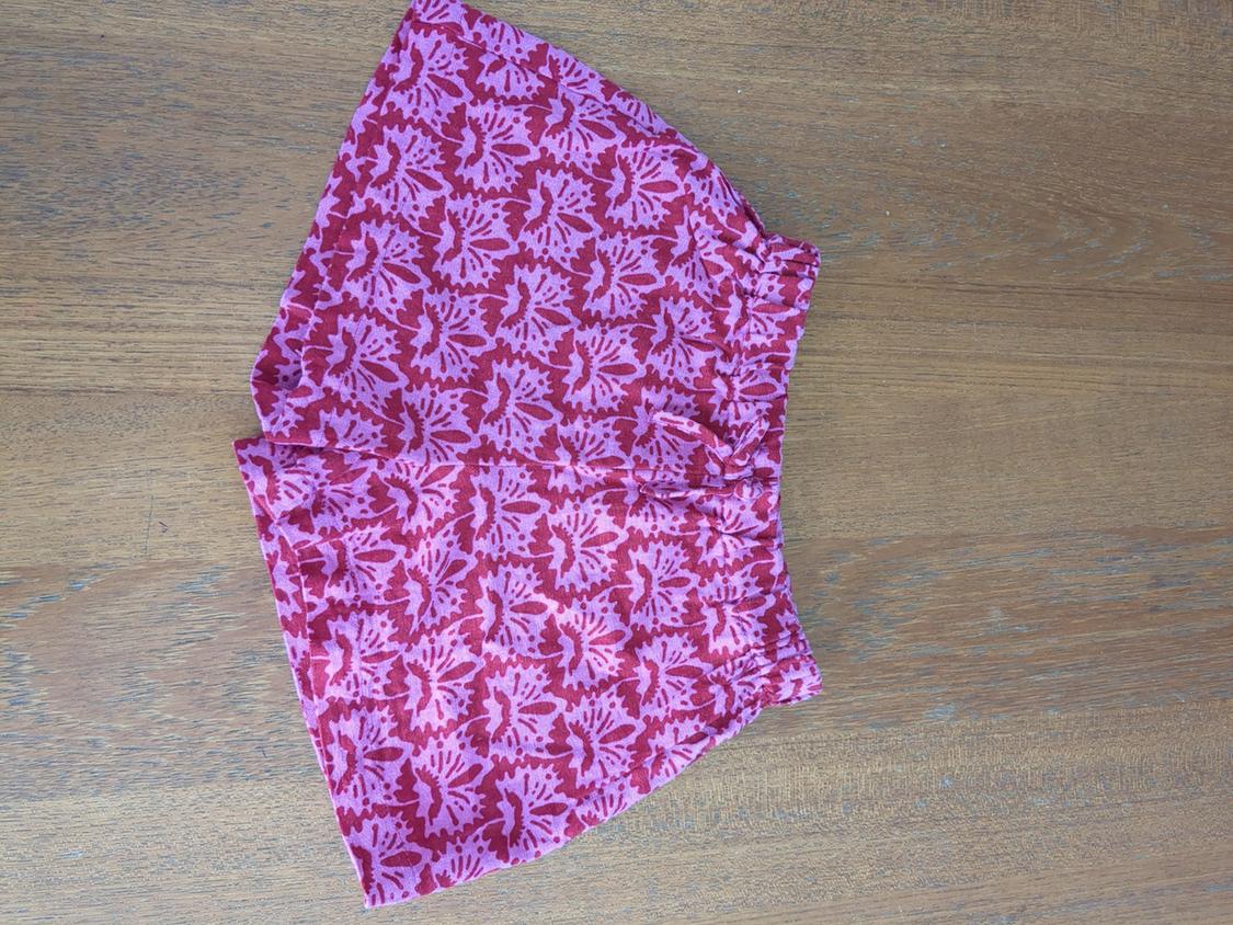 Floral print shorts in pink and red tones on a light wood surface.