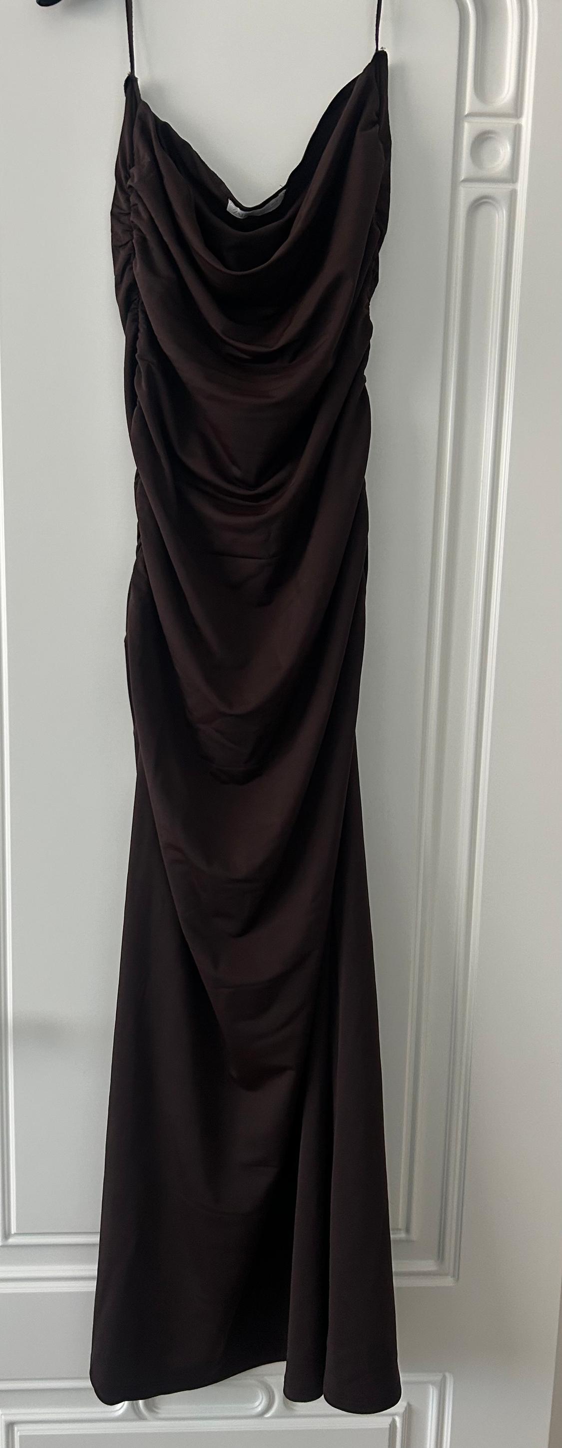 Long black dress with thin straps and a draped bust, hanging on a white door with decorative mouldings.