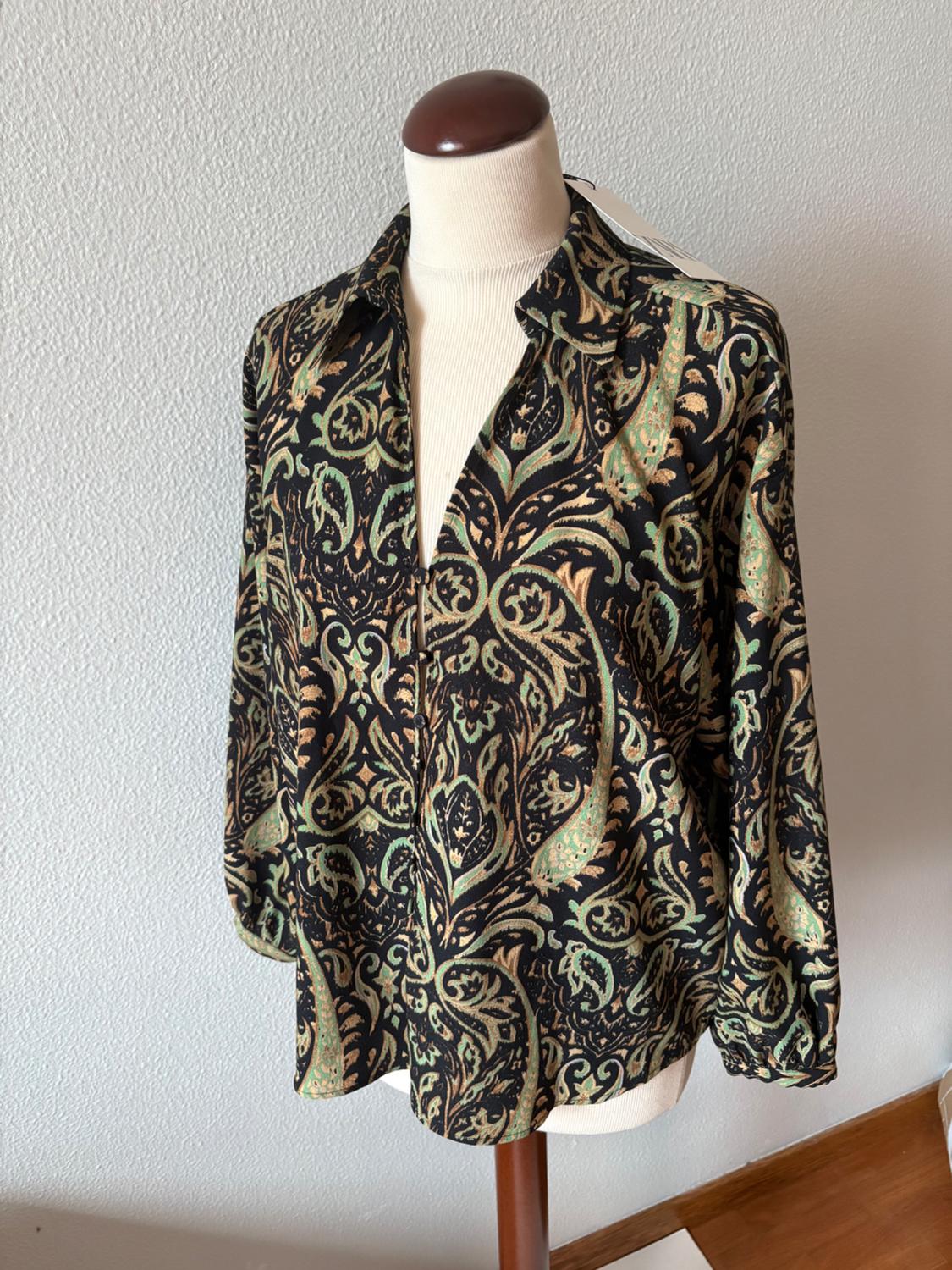 Black, green and gold paisley print long-sleeved button-up shirt on a mannequin, in front of a white wall.