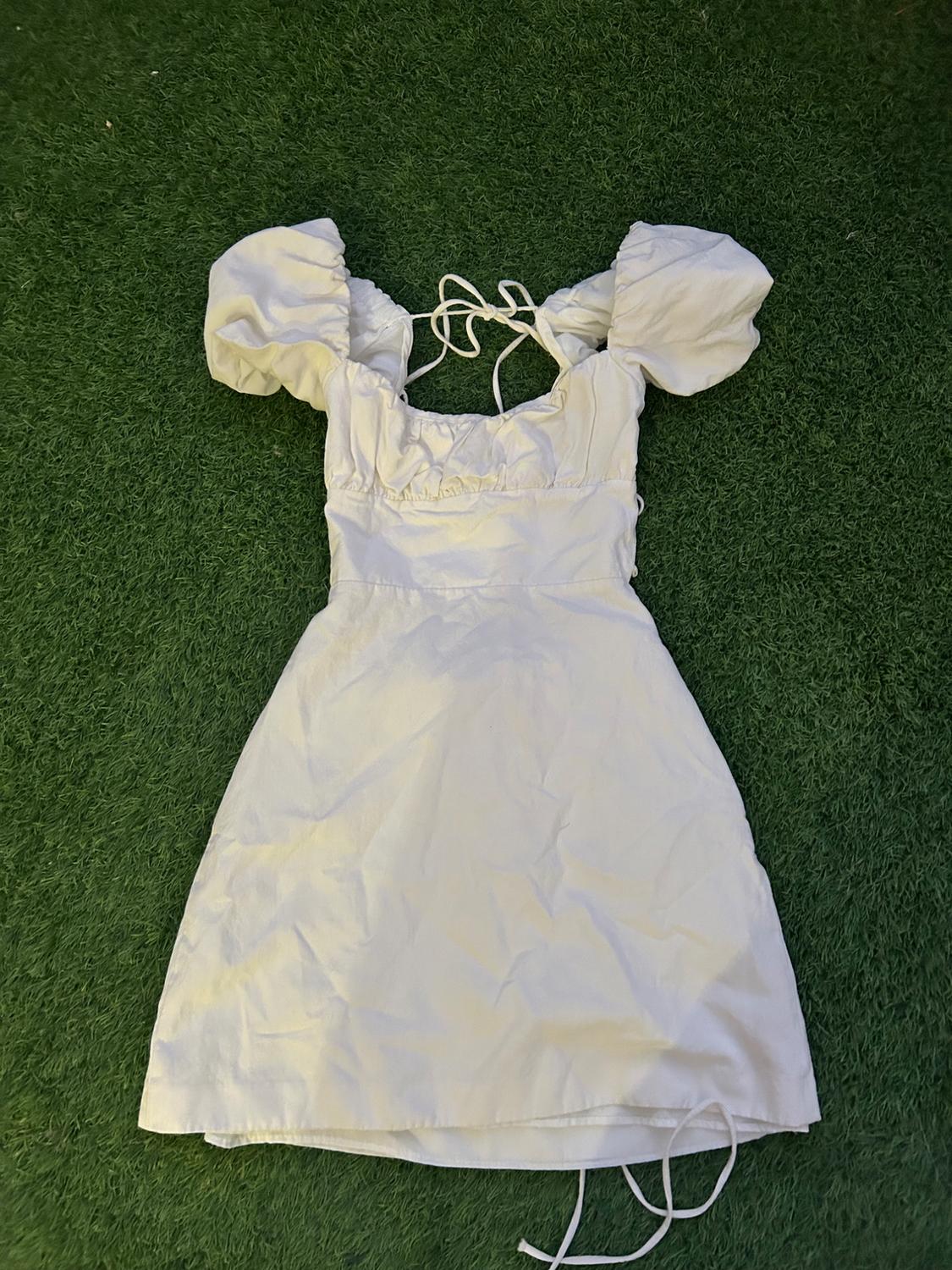 White dress with puffed sleeves and spaghetti straps, laid out on green grass.