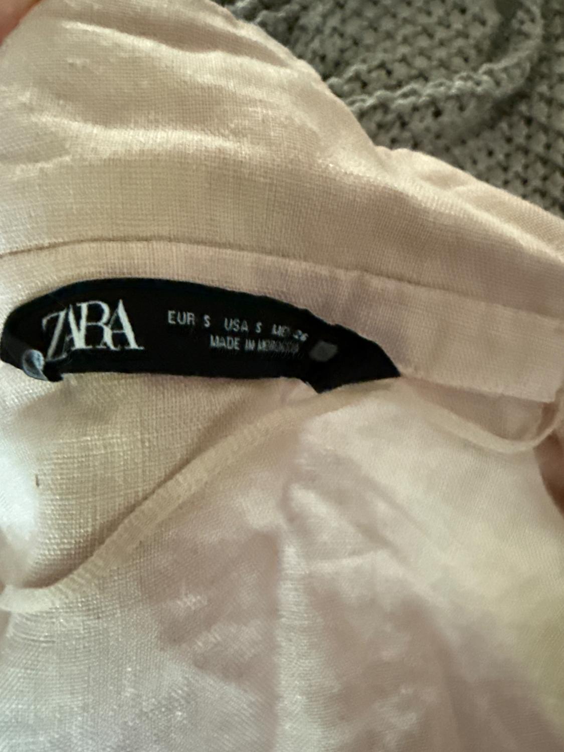 ZARA clothing tag on beige fabric, showing sizes EUR S, USA S, MEX 26 and "MADE IN ARMENIA" on a black background.