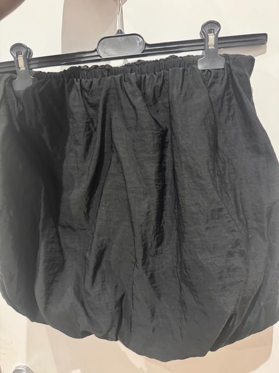 Black skirt with a crinkled texture hanging on a black hanger against a white background.