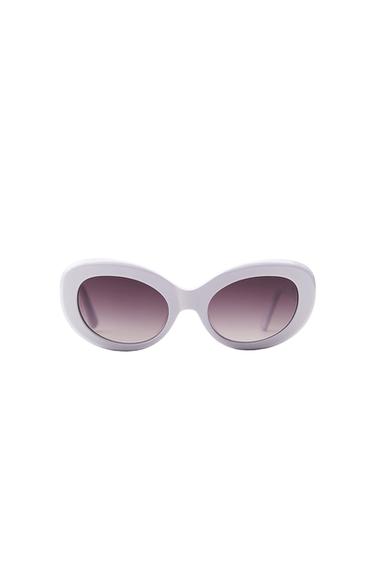 Sunglasses with thick white frames in an oval design and gradient lenses. Minimalist composition on a solid white background.