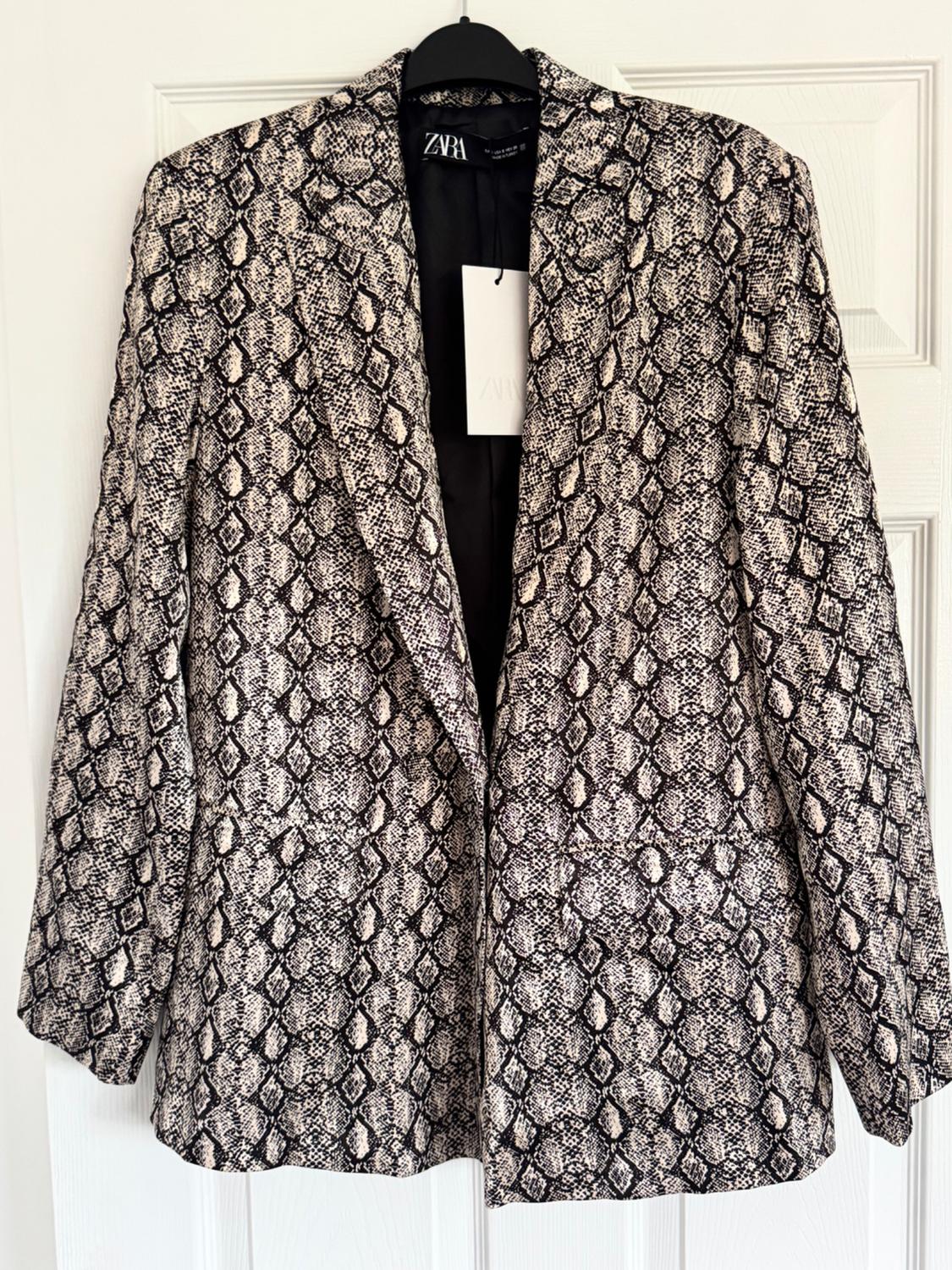 Blazer with snake print in beige and black tones, hanging on a black hanger. Label visible with the Zara logo.