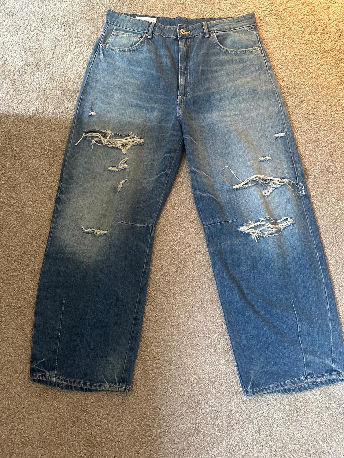 Distressed blue jeans with rips on the legs, placed on a beige rug.