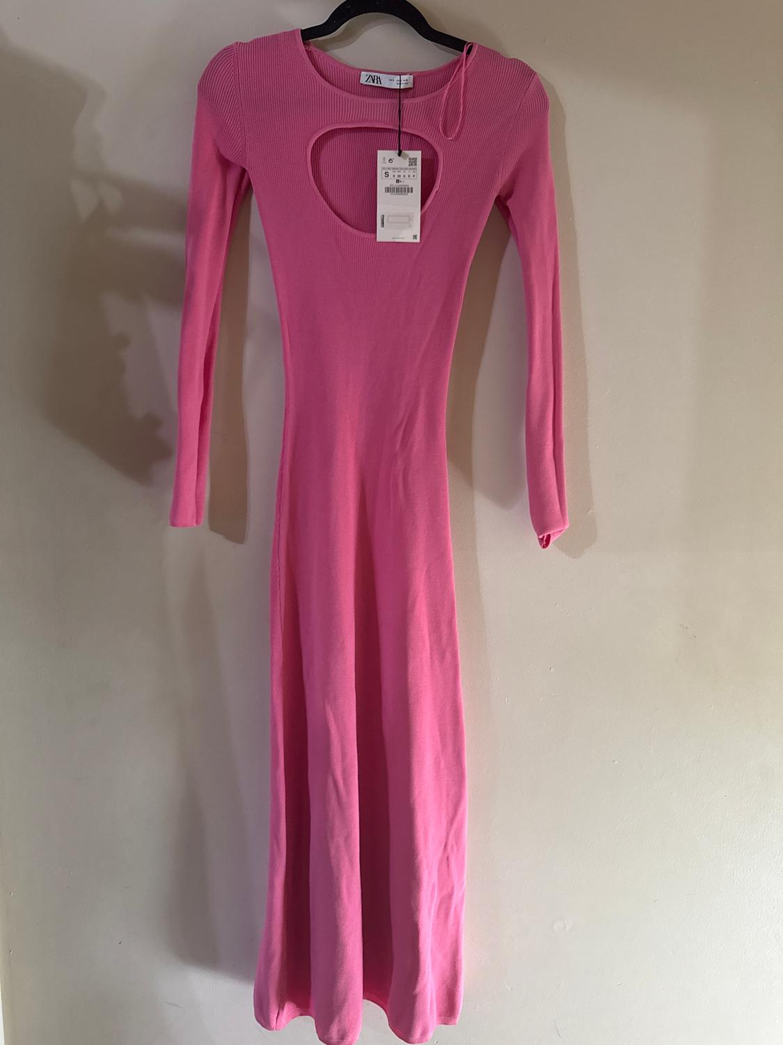 Long pink dress with a chest cutout, long sleeves, hanging on a black hanger. Visible tag with size and price details.