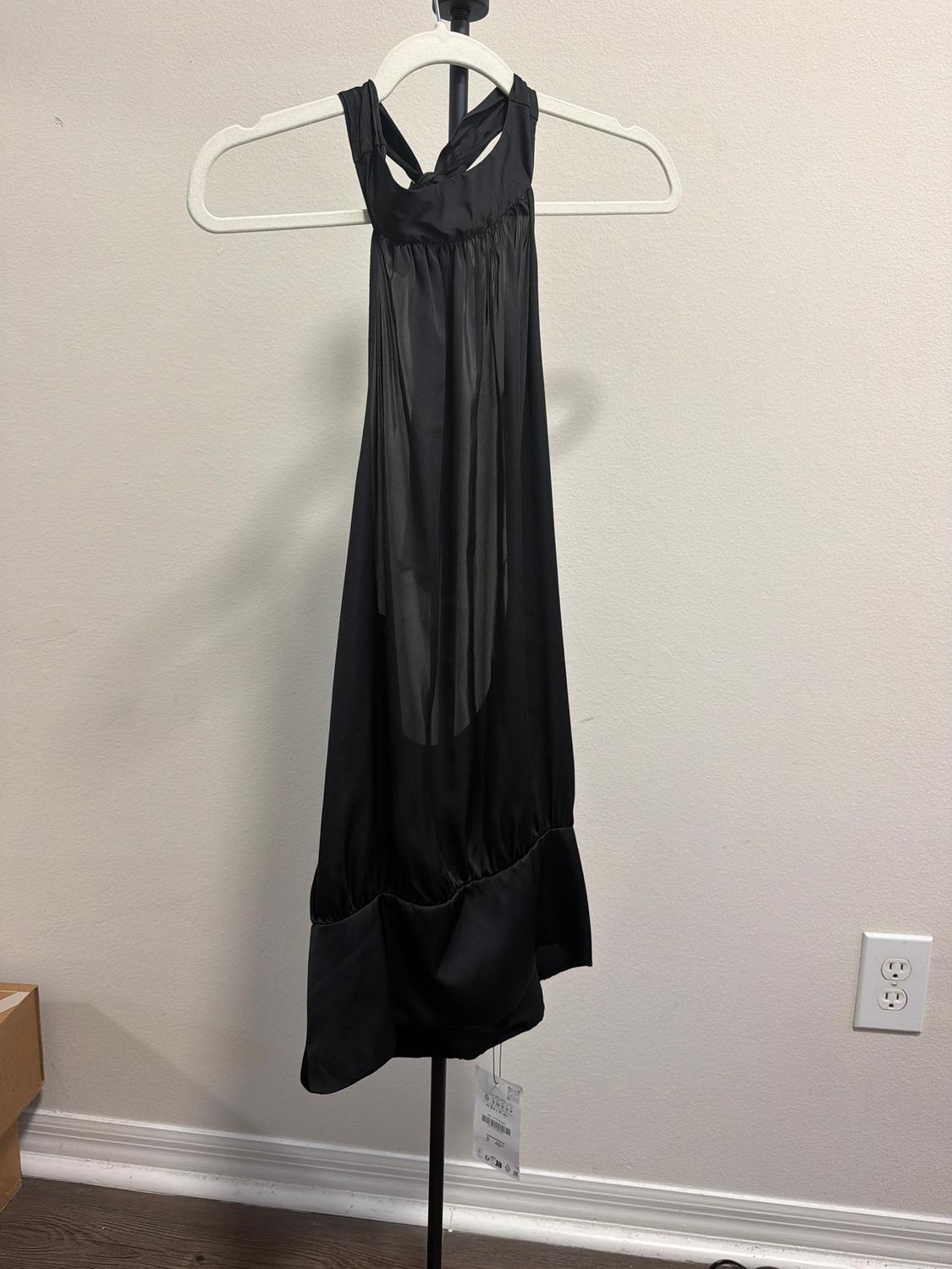 Sleeveless black dress hanging on a white hanger against a light background. The tag hangs from the bottom hem.