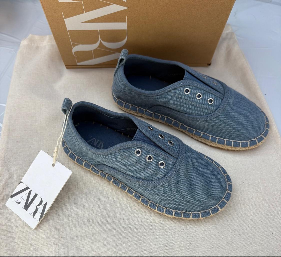 Blue canvas espadrilles with an espadrille sole, Zara tag and a cardboard box in the background on beige fabric.