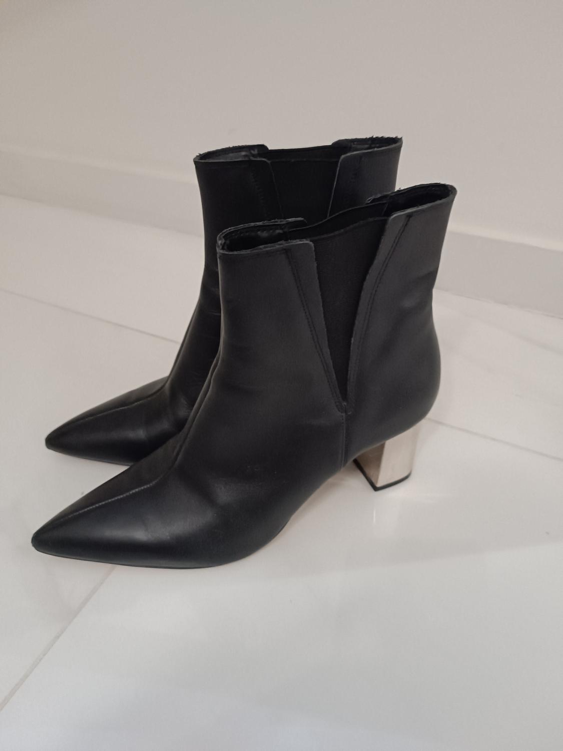 Black pointed ankle boots with a silver block heel on a white floor. Modern and minimalist style.