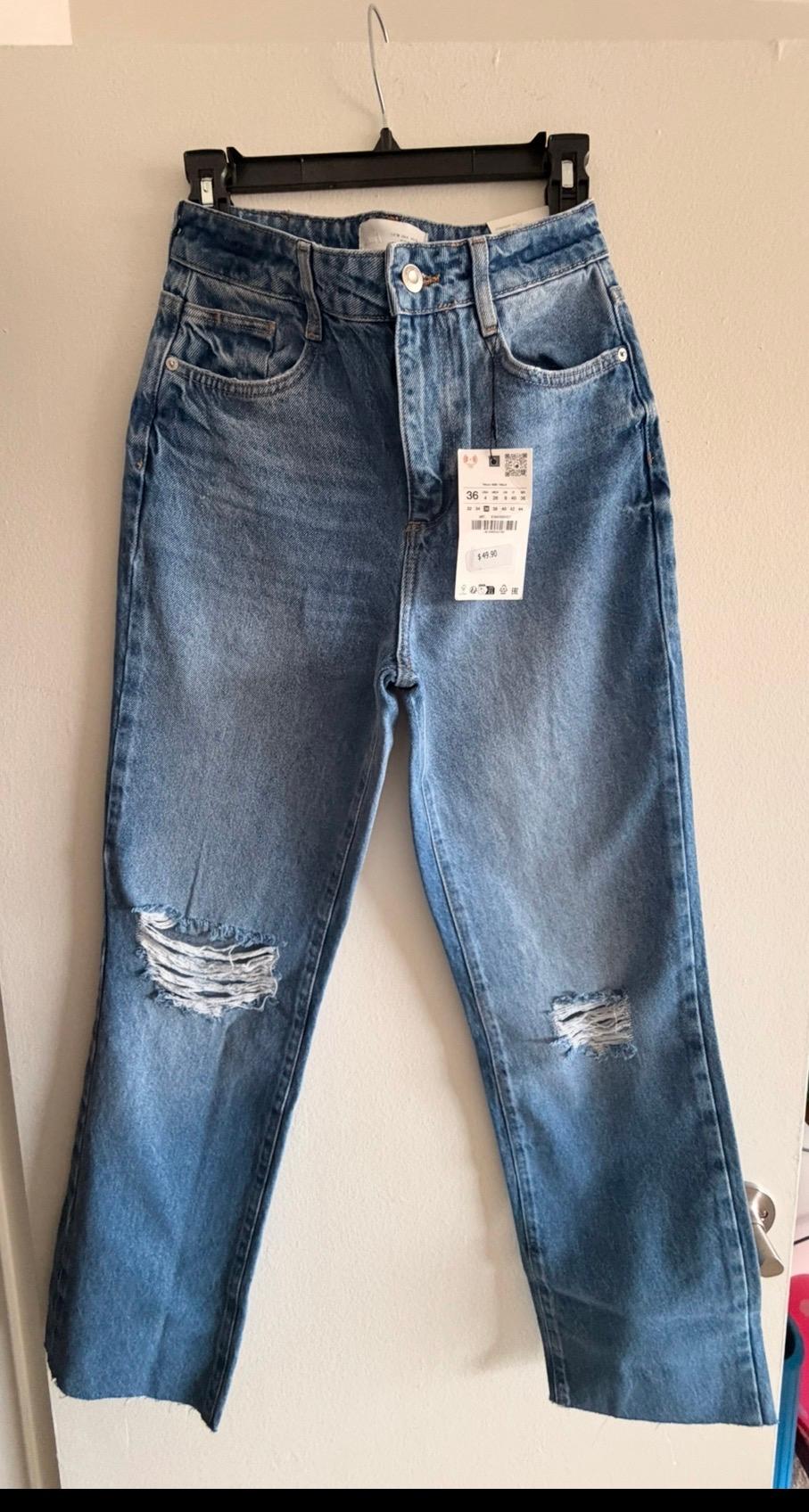 Worn blue jeans hanging on a black hanger, with price tag visible. White background.
