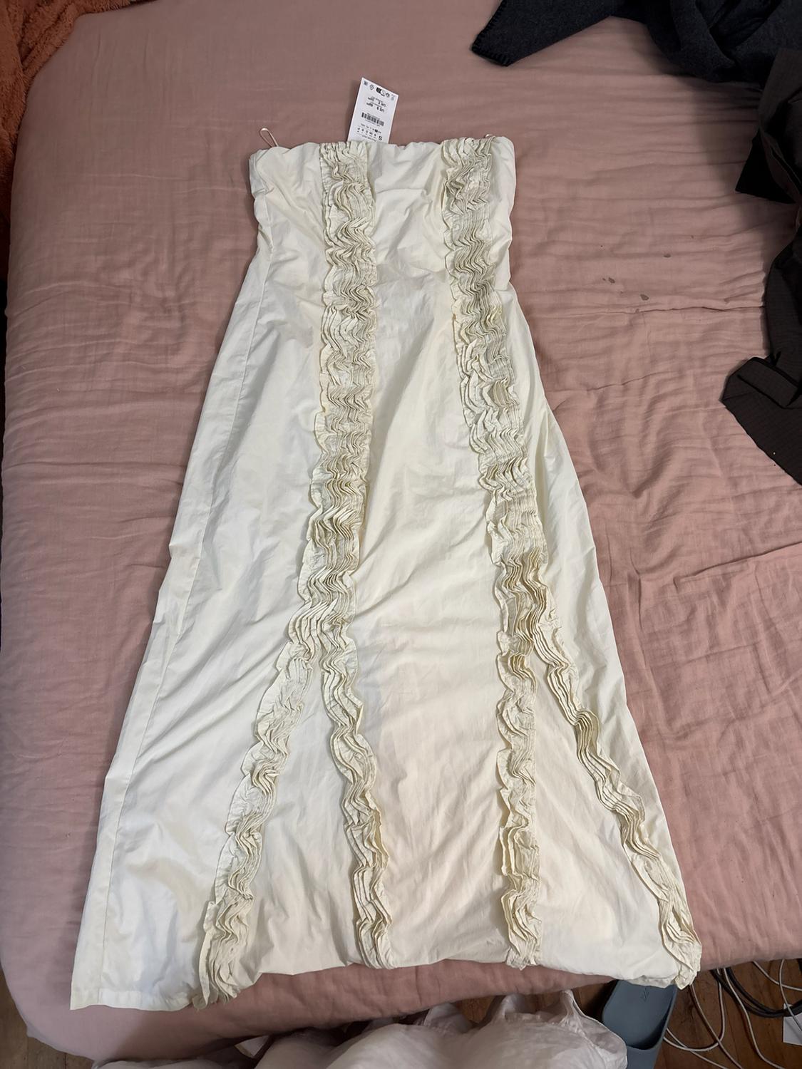 Long white strapless dress with vertical ruffle detailing, spread out on a bed with pink sheets.