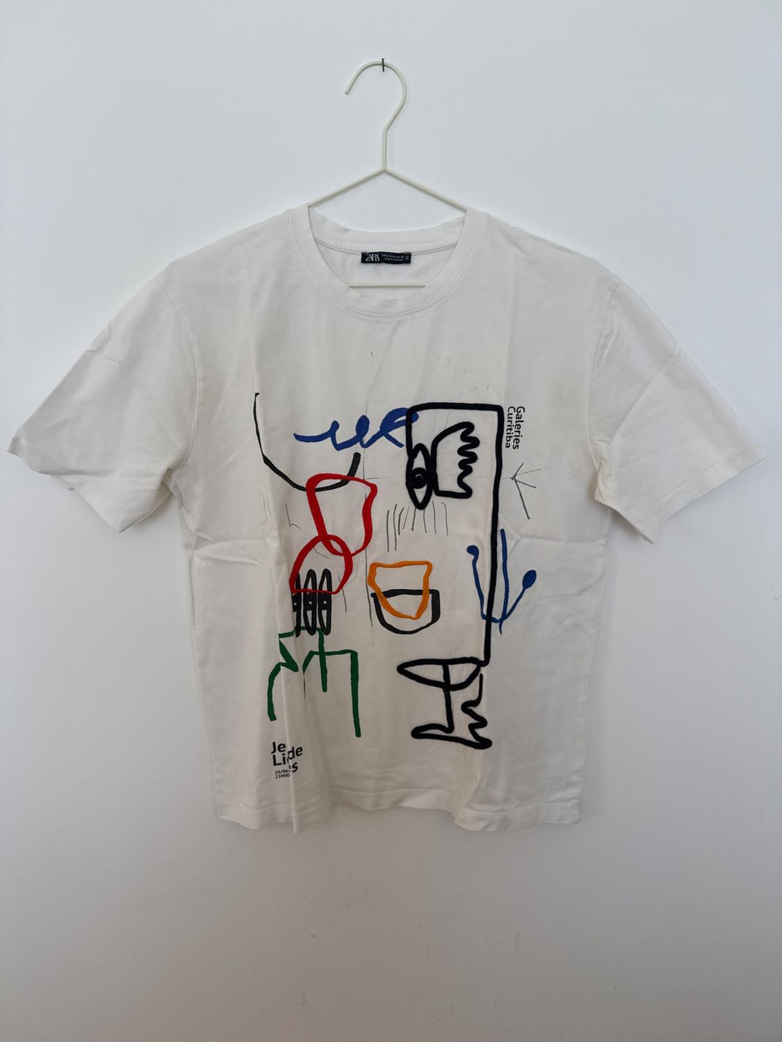Λευκό T-shirt σε κρεμάστρα με αφηρημένο τύπωμα από γραμμές και το κείμενο "Galeries Curitiba", "Je Lide s", "24/06/ 21H00".