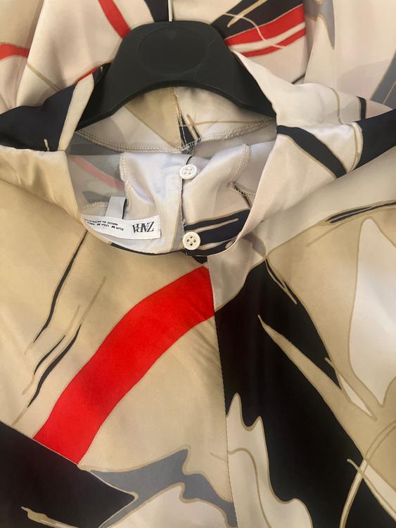 Patterned shirt with abstract designs in beige, black, and red, hanging on a black hanger. Visible label with text "ZARA".