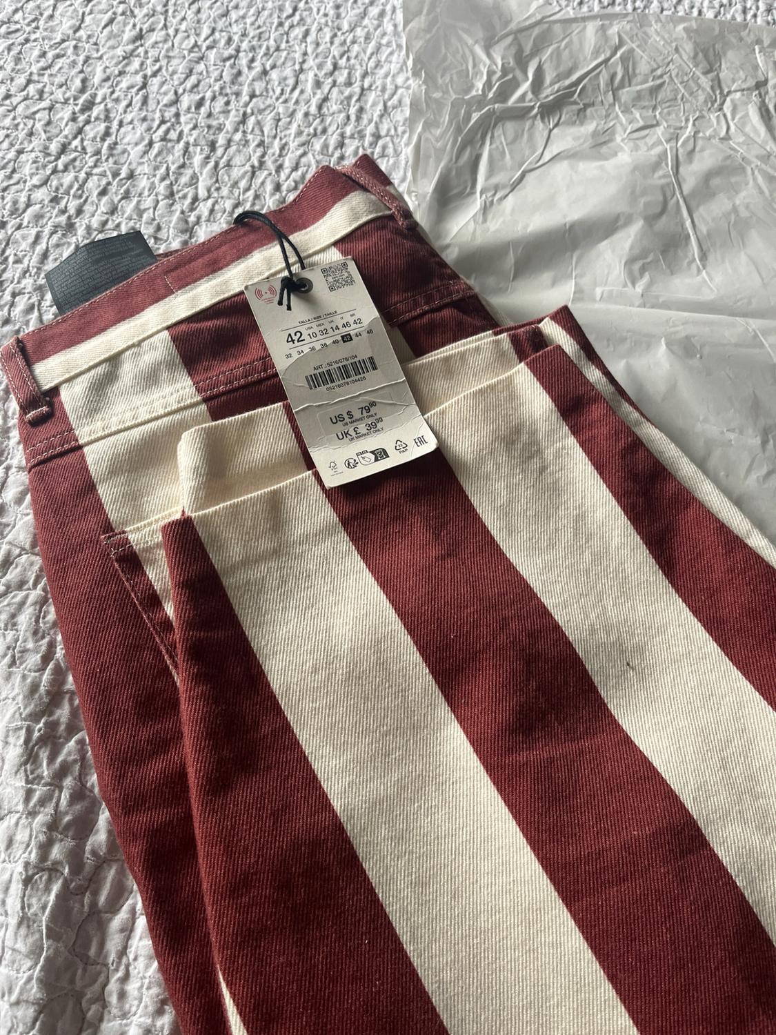 Maroon and white striped trousers folded on a bedspread with tissue paper. Label with text: 42 US $ 79.90 UK £ 39.99.