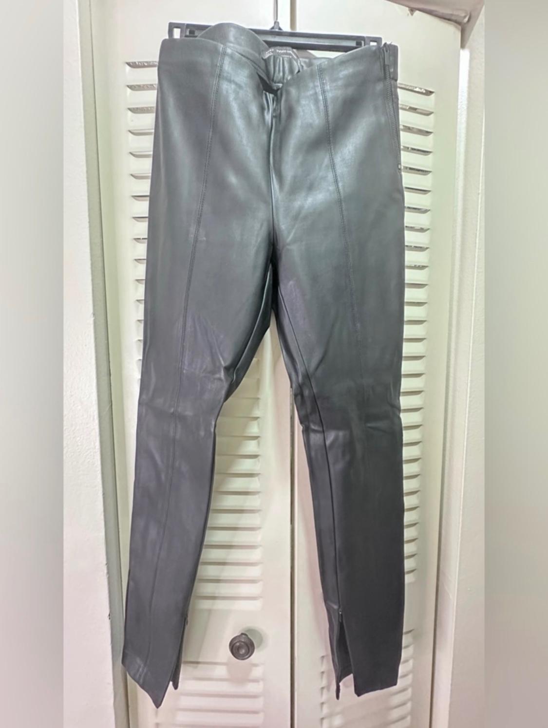 Black leather trousers hanging on a hanger in front of a white door with blinds.