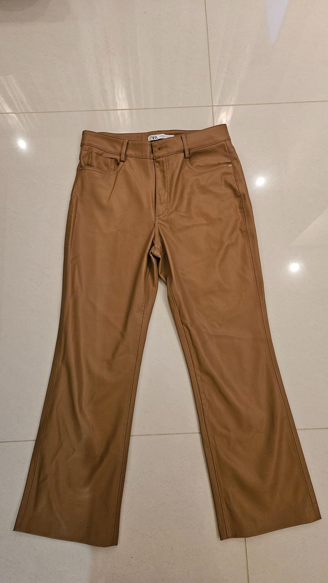 Brown straight-cut trousers on a light-coloured floor. Visible label on the waistband with the text "ZARA".