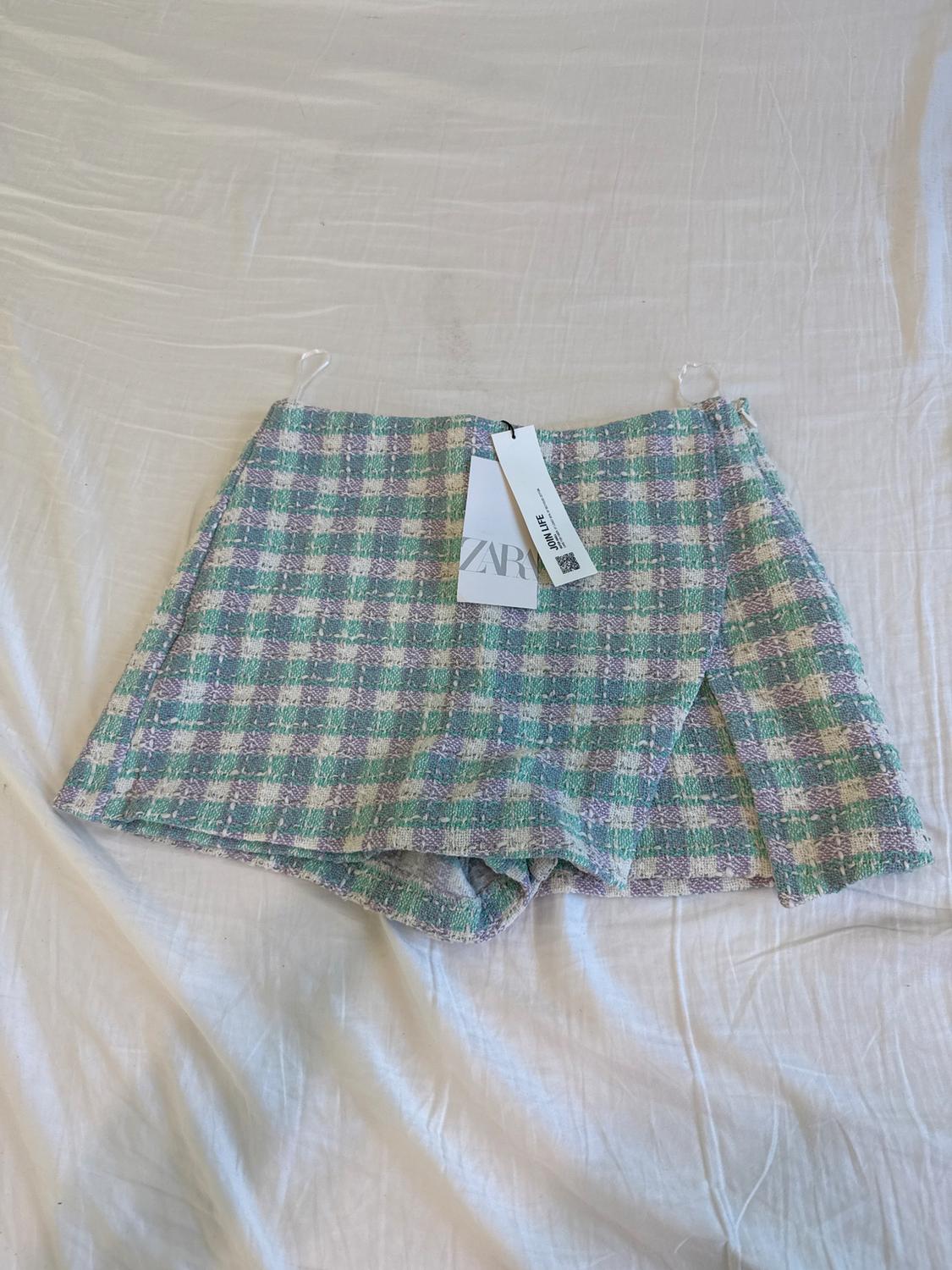 Checked fabric shorts in pastel colors on a white sheet. Visible tag with the text "ZARA".