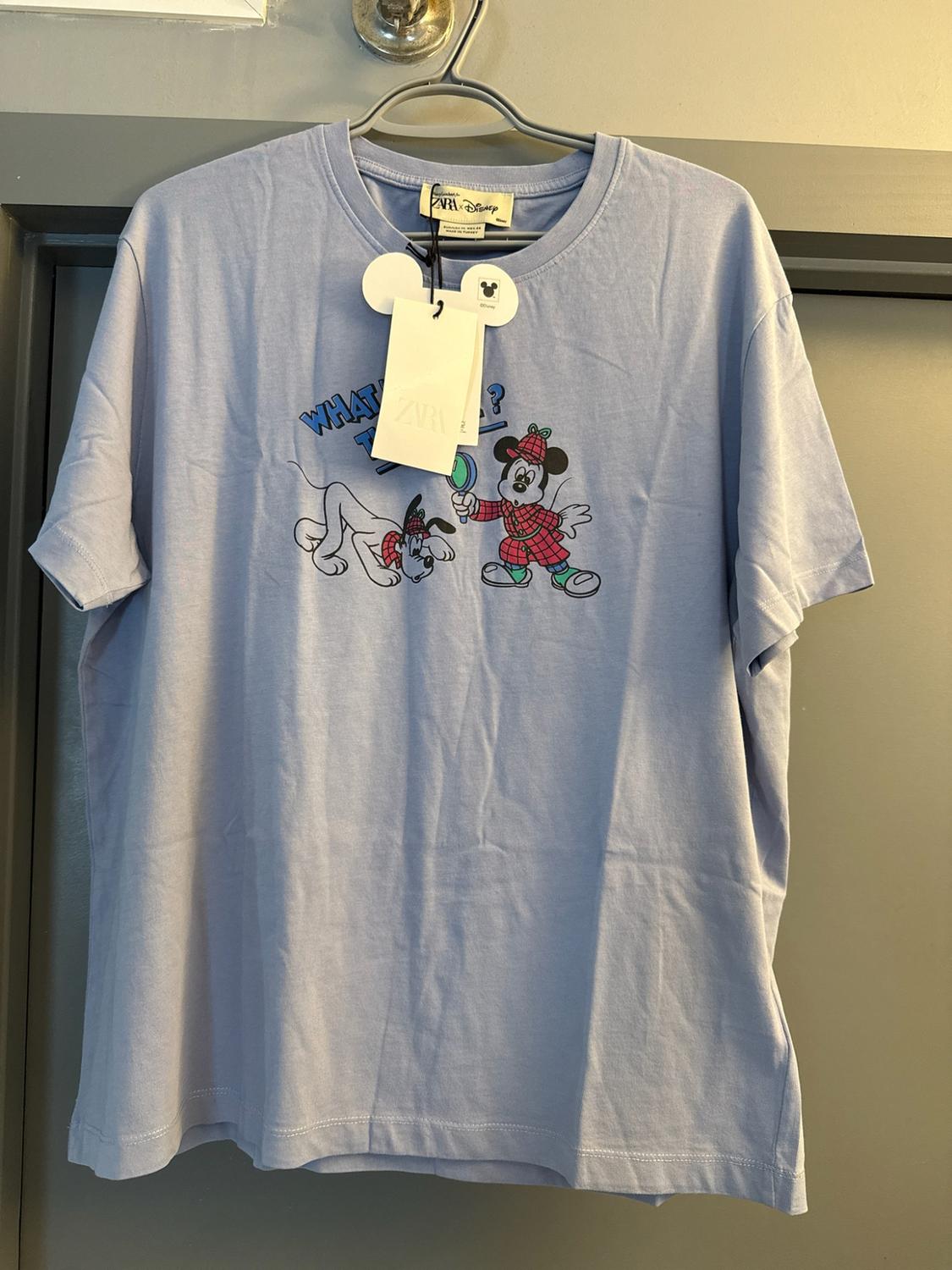 Light blue short-sleeved T-shirt on a hanger. Mickey Mouse and Pluto print. Text: WHAT, ?, ZARA, ZARA Disney.