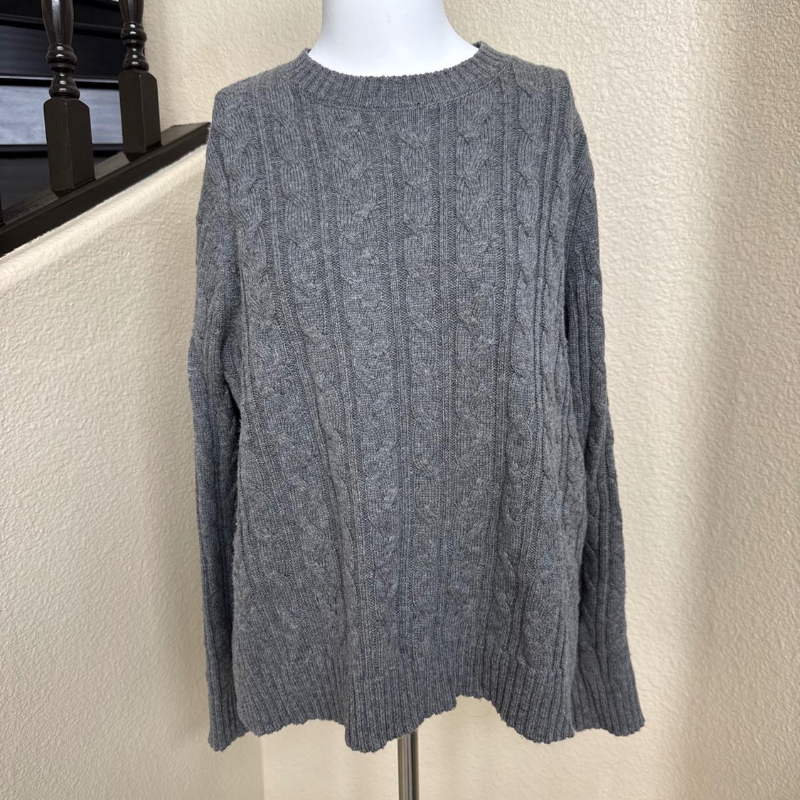 Gray cable-knit sweater on a white mannequin. Relaxed indoor setting with a beige wall and a dark wood staircase. Casual style.