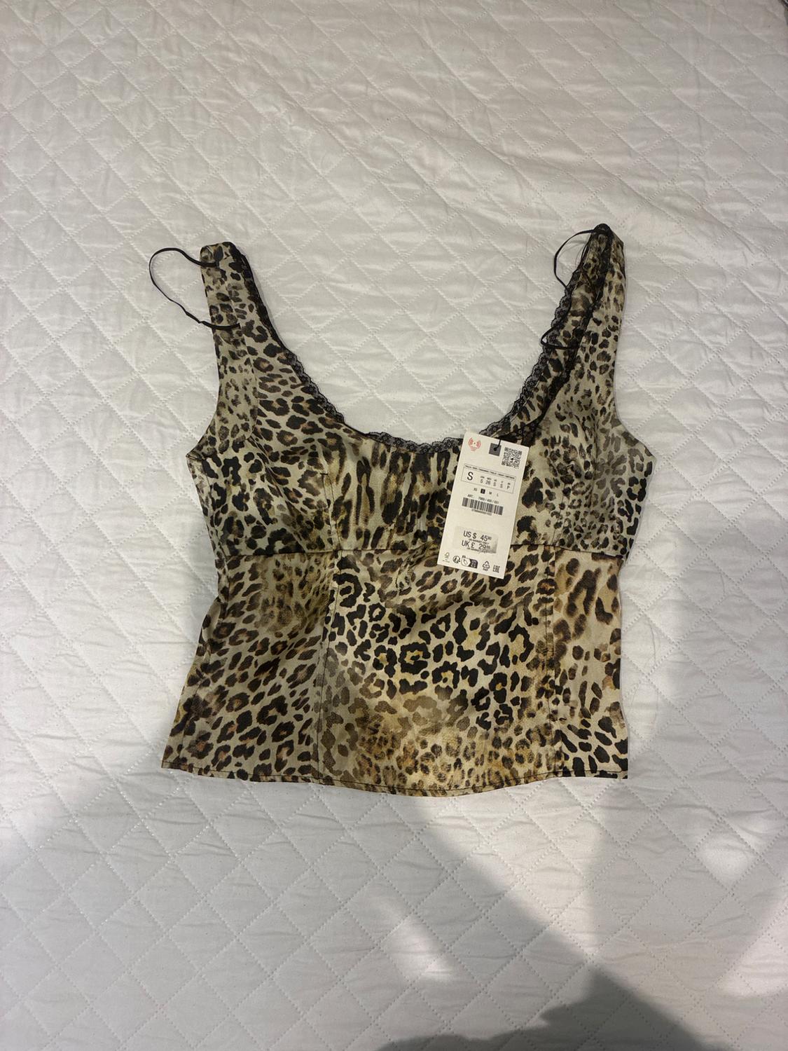 Leopard print camisole top on a white quilted bedspread. Visible tag with size and price details.