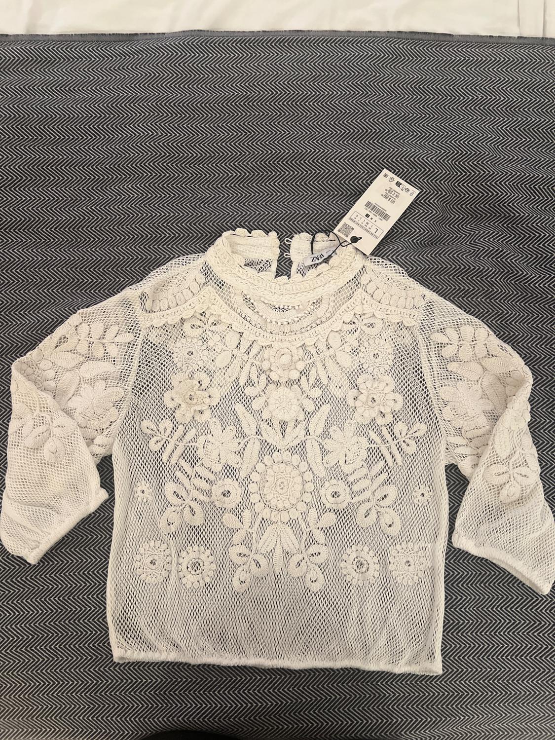 White mesh top with floral embroidery extended over a grey fabric with a zigzag pattern, relaxed fit. Text: ZARA.