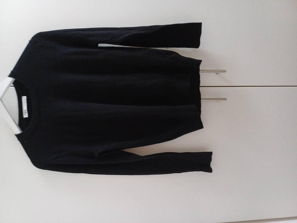 Black long-sleeved jumper hanging on a white hanger against a white background. Label visible on the collar.