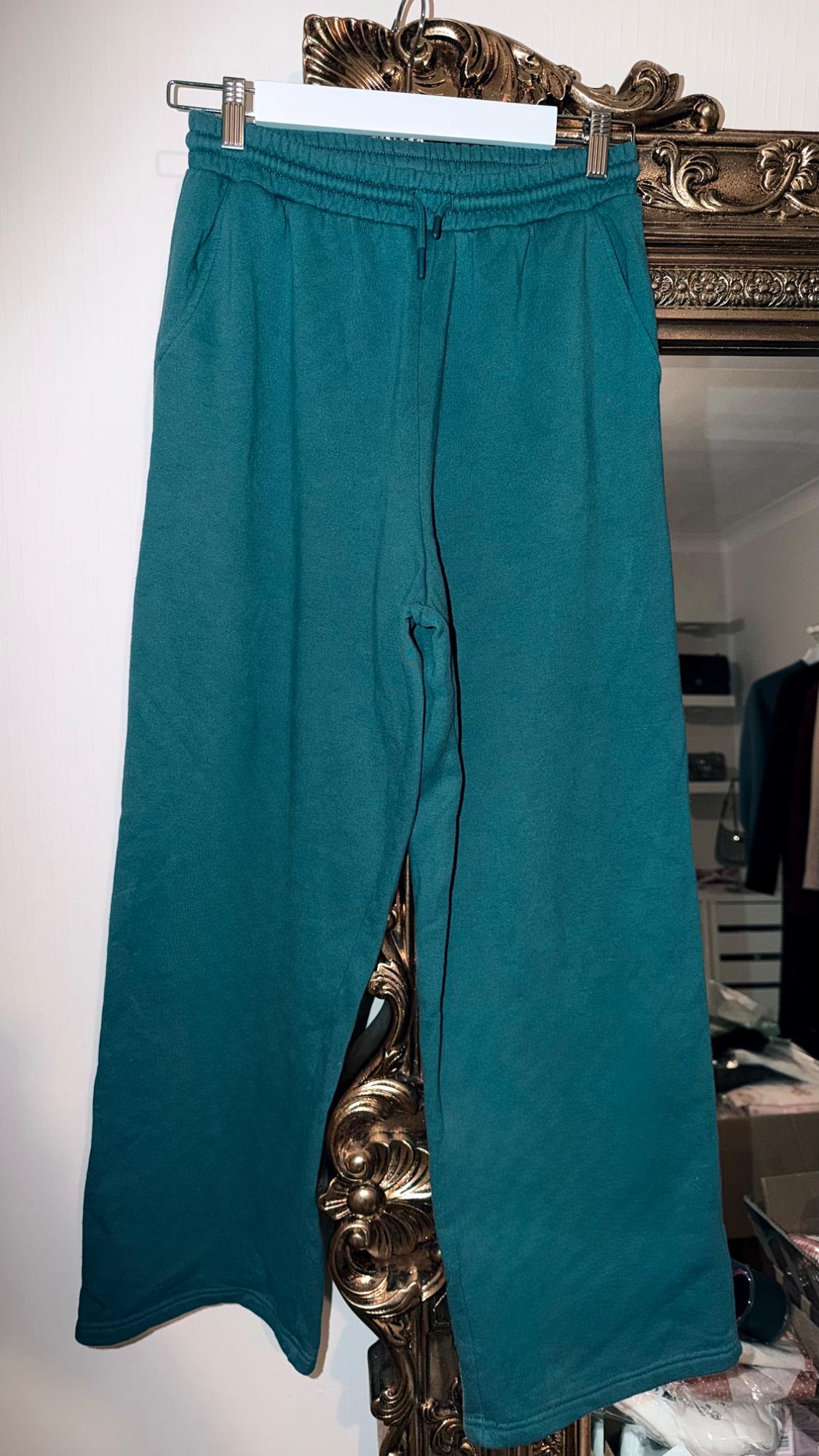 Green trousers hanging on a hanger in front of an ornate gold-framed mirror. Room background with clothes and shelves.
